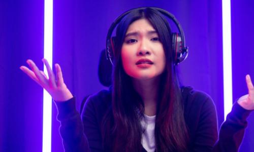Chinese woman gamer with headphones on looking bewildered into the camera