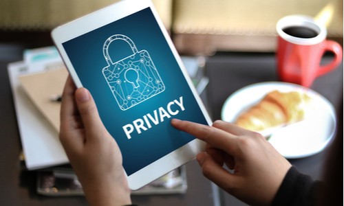 person holding a tablet with a digital picture of a padlock indicating online security, with coffee and a roll in the background