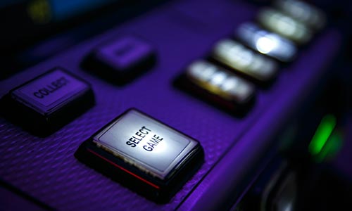 A blurry close-up image of a game machine with clunky buttons with the focus on the ‘select game’ button