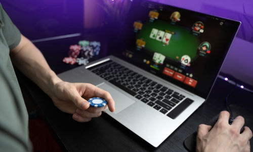 a gamer playing at an online casino screen on his laptop, holding casino chips