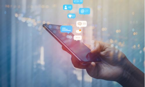 a hand using a mobile phone with icons of social channels floating around